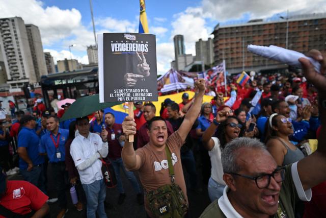 A demonstrator holds a banner during a march in Caracas on January 13, 2026, to demand the release of deposed Venezuelan president Nicolas Maduro and his wife Cilia Flores, snatched and taken to New York on January 3 to face trial on drug and weapons charges. Venezuela is working to identify the ‘human remains’ found after the United States attack that led to the fall of Nicolas Maduro and left around one hundred dead, Interior Minister Diosdado Cabello said on January 13,2026. (Photo by Juan BARRETO / AFP)
