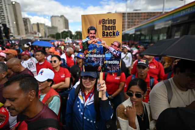 A demonstrator holds a banner during a march in Caracas on January 13, 2026, to demand the release of deposed Venezuelan president Nicolas Maduro and his wife Cilia Flores, snatched and taken to New York on January 3 to face trial on drug and weapons charges. Venezuela is working to identify the ‘human remains’ found after the United States attack that led to the fall of Nicolas Maduro and left around one hundred dead, Interior Minister Diosdado Cabello said on January 13,2026. (Photo by Juan BARRETO / AFP)