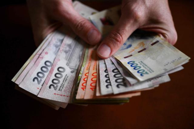 (FILES) A man holds Argentine pesos bills in Buenos Aires, on July 14, 2025. Inflation in Argentina rose slightly in December after six consecutive months of increases but ended 2025 at 31.5% compared to December of the previous year, its lowest level in eight years, the national statistics institute (Indec) reported on January 13, 2026. (Photo by Luis ROBAYO / AFP)