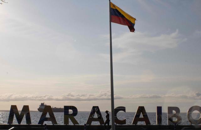 A woman walks in front of a sign reading 'Maracaibo' and a crude oil tanker anchored on Maracaibo Lake in Maracaibo, Venezuela on January 13, 2026. After the US raid that deposed Nicolas Maduro as Venezuela's leader, citizens hope the ensuing talks on selling its oil to US may improve their dire economic fortunes. (Photo by Margioni BERMÚDEZ / AFP)