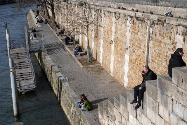 People sit on the docks of the Seine river at the Ile de la Cite in central Paris, on January 13, 2026. (Photo by Martin LELIEVRE / AFP)