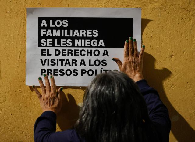 A woman puts up a poster on the wall during a vigil to demand freedom for political prisoners at El Helicoide -a facility and prison owned by the Venezuelan government and used for both regular and political prisoners of the Bolivarian National Intelligence Service (SEBIN)- in Caracas on January 13, 2026. Venezuela said on January 12, it had freed dozens more political prisoners as rights groups questioned the numbers and family members clamored for speedier releases after the US military ouster of long-term autocrat Nicolas Maduro. (Photo by Pedro MATTEY / AFP)