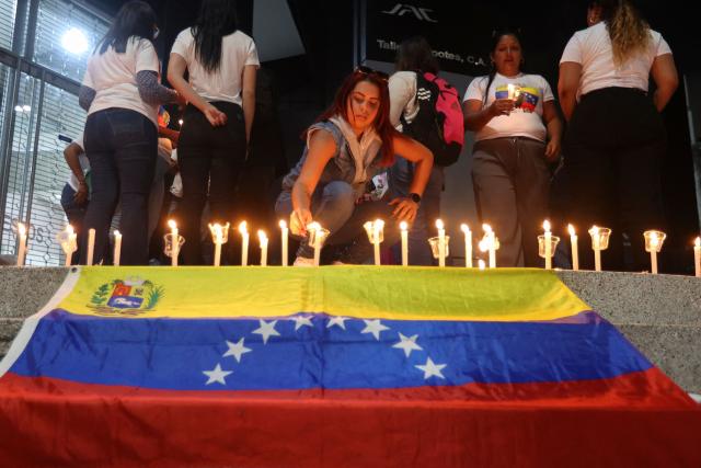A woman lit a candle next to a Venezuelan flag during a vigil to demand freedom for political prisoners at El Helicoide -a facility and prison owned by the Venezuelan government and used for both regular and political prisoners of the Bolivarian National Intelligence Service (SEBIN)- in Caracas on January 13, 2026. Venezuela said on January 12, it had freed dozens more political prisoners as rights groups questioned the numbers and family members clamored for speedier releases after the US military ouster of long-term autocrat Nicolas Maduro. (Photo by Pedro MATTEY / AFP)