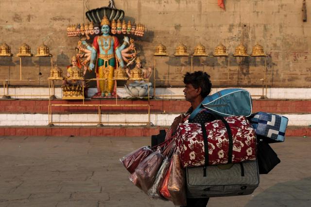 A vendor selling bags walks past a statue of Hindu deity Krishna, as he looks for customers at Chauki Ghat along the banks of river Ganges in Varanasi on January 14, 2026. (Photo by Niharika KULKARNI / AFP)