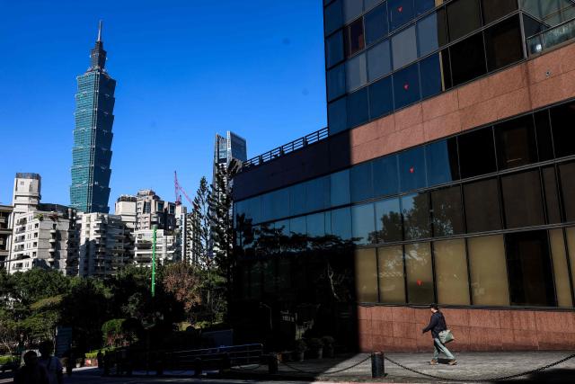 A pedestrian walks along a footpath as the landmark Taipei 101 building is seen in the background in Taipei on January 14, 2026. (Photo by I-Hwa Cheng / AFP)