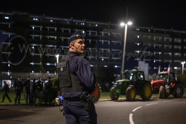A french riot police officer stands in front of tractors parked outside Toulouse airport in Toulouse, southwestern France on January 14, 2026 in protest against the government's mandatory culling protocol for cattle herds affected by lumpy skin disease (dermatose nodulaire contagieuse) and the EU-Mercosur trade deal. (Photo by Ed JONES / AFP)