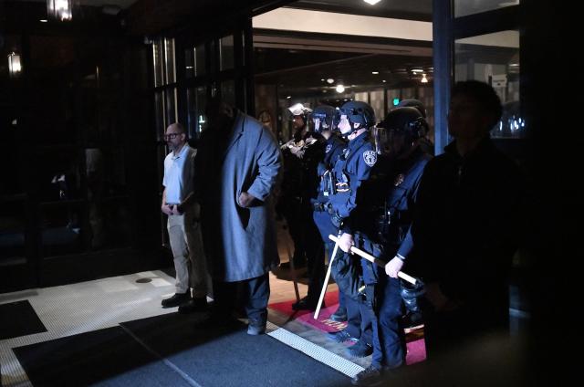 Local law enforcement stand at the entrance of the Graduate Hotel where federal immigration agents are believed to be staying as anti-ICE demonstrators protest outside in Minneapolis, Minnesota on January 13, 2026. Hundreds more federal agents were heading to Minneapolis, the US homeland security chief said on January 11, brushing aside demands by the Midwestern city's Democratic leaders to leave after an immigration officer fatally shot a woman protester. In multiple TV interviews, US Homeland Secretary Kristi Noem defended the actions of the officer who shot and killed 37-year-old Renee Nicole Good, whose death has sparked renewed protests nationwide against President Donald Trump's immigration crackdown. (Photo by Octavio JONES / AFP)