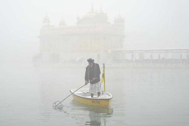 A Sikh volunteer cleans the holy lake on the occasion of Maghi festival or Makar Sankranti, amid dense fog at the Golden Temple in Amritsar on January 14, 2026. (Photo by Narinder NANU / AFP)