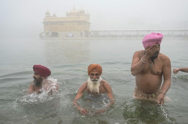 Sikh devotees take a dip in the holy lake on the occasion of Maghi festival or Makar Sankranti, amid dense fog at the Golden Temple in Amritsar on January 14, 2026. (Photo by Narinder NANU / AFP)