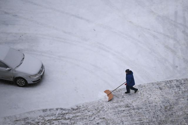 A worker clear snow in a parking lot in Kyiv on January 14, 2026, amid the Russian invasion of Ukraine. (Photo by Sergei GAPON / AFP)