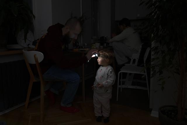TOPSHOT - Local resident Stas helps his two-year-old daughter use a headlight during a power outage at the family's apartment in Kyiv on January 13, 2026, amid the Russian invasion of Ukraine. (Photo by Andrew Kravchenko / AFP)
