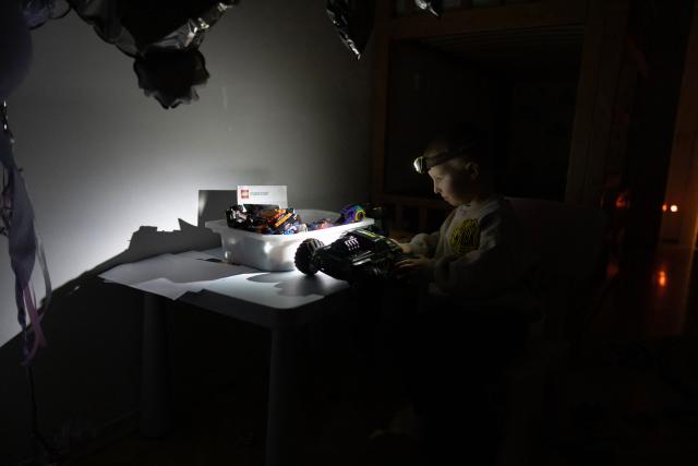 Local residents Stas and Kateryna's five-year-old son uses a headlight as he plays with a toy car during a power outage at the family's apartment in Kyiv on January 13, 2026. (Photo by Andrew Kravchenko / AFP)