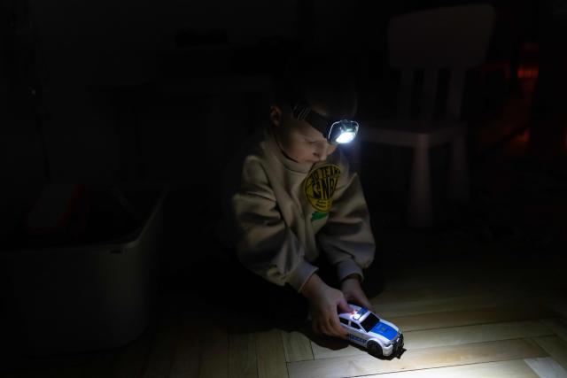 Local residents Stas and Kateryna's five-year-old son uses a headlight as he plays with a toy car during a power outage at the family's apartment in Kyiv on January 13, 2026. (Photo by Andrew Kravchenko / AFP)