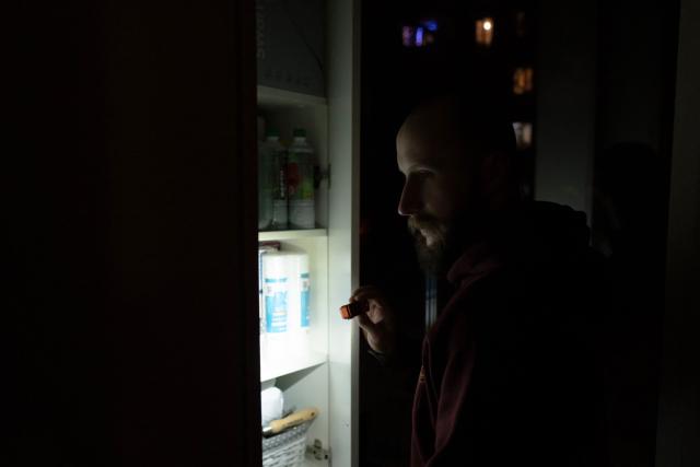 Local resident Stas uses a flashlight to look into a cabinet during a power outage at the family's apartment in Kyiv on January 13, 2026, amid the Russian invasion of Ukraine. (Photo by Andrew Kravchenko / AFP)