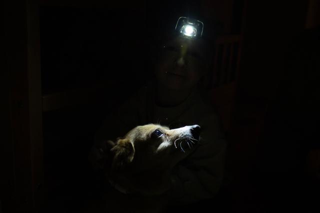 Local residents Stas and Kateryna's five-year-old son uses a headlight as he interacts with his dog Fistashka during a power outage at the family's apartment in Kyiv on January 13, 2026, amid the Russian invasion of Ukraine. (Photo by Andrew Kravchenko / AFP)