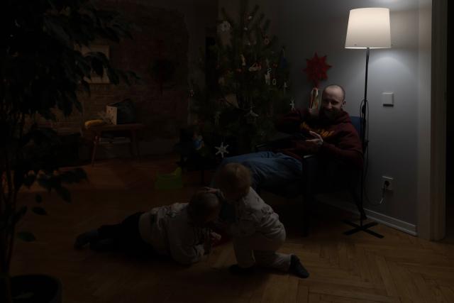 Local resident Stas spends time with his two children during a power outage at the family's apartment in Kyiv on January 13, 2026, amid the Russian invasion of Ukraine. (Photo by Andrew Kravchenko / AFP)