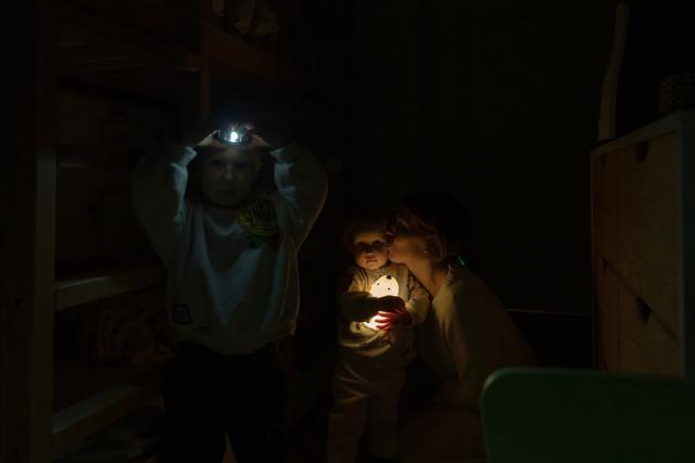 Local resident Kateryna spends time with her two children during a power outage at the family's apartment in Kyiv on January 13, 2026, amid the Russian invasion of Ukraine. (Photo by Andrew Kravchenko / AFP)