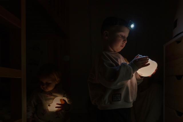 Local residents Stas and Kateryna's five-year-old son and two-year-old daughter play in their room before bedtime during a power outage at the family's apartment in Kyiv on January 13, 2026, amid the Russian invasion of Ukraine. (Photo by Andrew Kravchenko / AFP)