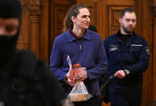 The defendant, German anti-fascist activist Maja T, is lead into the courtroom in handcuffs and on a leash by an official in Budapest on January 14, 2026 to expect his verdict for allegedly participating in attacks against presumed neo-Nazis on the streets of the Hungarian capital. The case sparked uproar in Germany, with the country's top court saying the extradition order for the suspect, who identifies as non-binary, had failed to take into account potentially dangerous prison conditions in Hungary, especially for LGBTQ people. The defendant is accused of four counts of attempted assault as part of a criminal organisation aiming to "send a deterrent message to members of extreme-right movements" by "inflicting various life-threatening injuries" according to a court statement. (Photo by Attila KISBENEDEK / AFP) / EDITORS NOTE: ACCORDING TO COURT'S RULING THE FACES OF THE JUSTICE OFFICERS AND POLICE IN THE COURTROOM MUST BE MADE UNRECOGNIZABLE