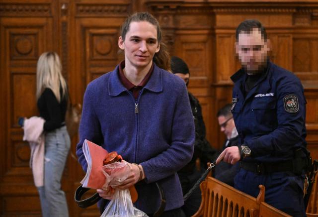 The defendant, German anti-fascist activist Maja T, is lead into the courtroom in handcuffs and on a leash by an official in Budapest on January 14, 2026 to expect his verdict for allegedly participating in attacks against presumed neo-Nazis on the streets of the Hungarian capital. The case sparked uproar in Germany, with the country's top court saying the extradition order for the suspect, who identifies as non-binary, had failed to take into account potentially dangerous prison conditions in Hungary, especially for LGBTQ people. The defendant is accused of four counts of attempted assault as part of a criminal organisation aiming to "send a deterrent message to members of extreme-right movements" by "inflicting various life-threatening injuries" according to a court statement. (Photo by Attila KISBENEDEK / AFP) / EDITORS NOTE: ACCORDING TO COURT'S RULING THE FACES OF THE JUSTICE OFFICERS AND POLICE IN THE COURTROOM MUST BE MADE UNRECOGNIZABLE