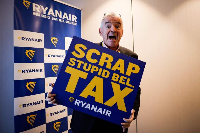 Irish budget Chief executive of lowcost airline Ryanair, Michael O'Leary poses with a sign reading "Scrap stupid Bel. tax" referring to Belgium's "embarkation tax" ahead of a press conference in Brussels, on January 14, 2026. Ryanair announced on December 9, 2025, it was to cut "1 million seats and 20 routes from its Brussels Winter 2026-2027 schedule" following the increase of the Belgian "embarkation tax" usually referred to as the "flight-ticket tax". (Photo by Simon Wohlfahrt / AFP)