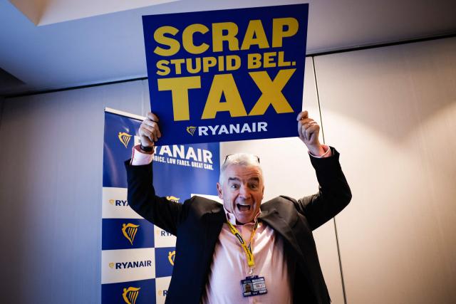 Irish budget Chief executive of lowcost airline Ryanair, Michael O'Leary poses with a sign reading "Scrap stupid Bel. tax" referring to Belgium's "embarkation tax" ahead of a press conference in Brussels, on January 14, 2026. Ryanair announced on December 9, 2025, it was to cut "1 million seats and 20 routes from its Brussels Winter 2026-2027 schedule" following the increase of the Belgian "embarkation tax" usually referred to as the "flight-ticket tax". (Photo by Simon Wohlfahrt / AFP)