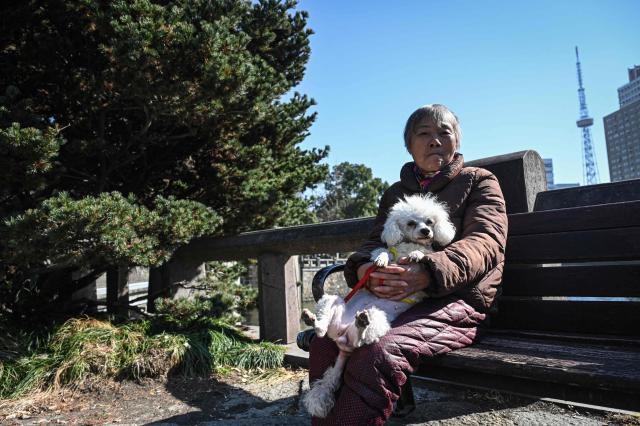 A woman holding a dog sits on a bench at a park in Hangzhou, in eastern China's Zhejiang province on January 14, 2026. (Photo by Jade GAO / AFP)