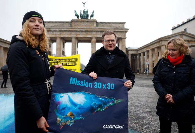 Greenpeace marine biologist Franziska Saalmann (L) and German Minister for the Environment, Climate Protection, Nature Conservation  and Nuclear Safety Carsten Schneider (C) hold a poster as former German Environment Minister Steffi Lemke (R) looks on during a demonstration for the protection of the oceans on January 14, 2026 in front of the Brandenburg Gate in Berlin, as the "Agreement under the United Nations Convention on the Law of the Sea on the Conservation and Sustainable Use of Marine Biological Diversity of Areas beyond National Jurisdiction (BBNJ Agreement)" is to enter into force. The agreement, also referred to as the High Seas Treaty or Global Ocean Treaty, is "the first legally binding agreement focused on conserving marine life on the High Seas", according to Greenpeace. (Photo by Odd ANDERSEN / AFP)
