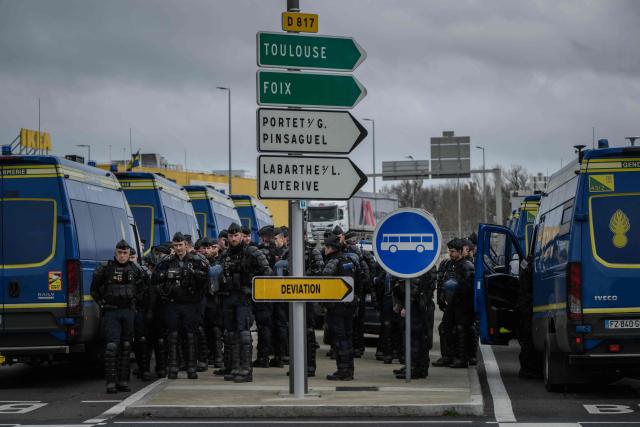 French Gendarmes stand by as farmers and their tractors gather on a roundabout on a road outside Toulouse in protest against the government's mandatory culling protocol for cattle herds affected by lumpy skin disease (dermatose nodulaire contagieuse) and the EU-Mercosur trade deal, in Toulouse, southwestern France on January 14, 2026. (Photo by Ed JONES / AFP)