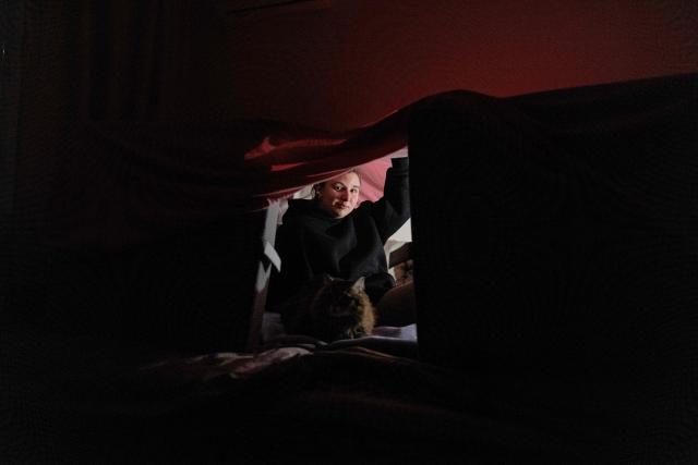 Local resident and piano teacher Evgenia sits with her cat under a tent built up inside her home and made of pillows and blankets in order to warm up, during a blackout in Kyiv, in the evening of January 13, 2026, amid the Russian invasion of Ukraine. (Photo by Tetiana DZHAFAROVA / AFP)