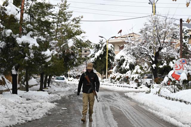 An armed man walks in the snow covered Syrian town of Bludan, some 50 kilometres northwest of the capital Damascus on January 14, 2026. (Photo by LOUAI BESHARA / AFP)