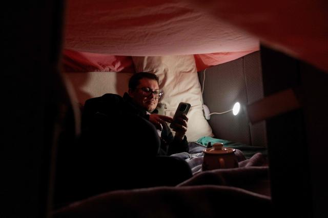 Local resident and Evgenia's husband Pavlo sits under a tent built up inside their home and made of pillows and blankets in order to warm up, during a blackout in Kyiv, in the evening of January 13, 2026, amid the Russian invasion of Ukraine. (Photo by Tetiana DZHAFAROVA / AFP)