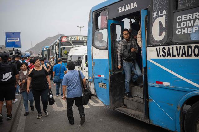People walk next to the bus crowding during a strike called by public transport companies against extortion and to demand greater security in Lima on January 14, 2026.  (Photo by ERNESTO BENAVIDES / AFP)
