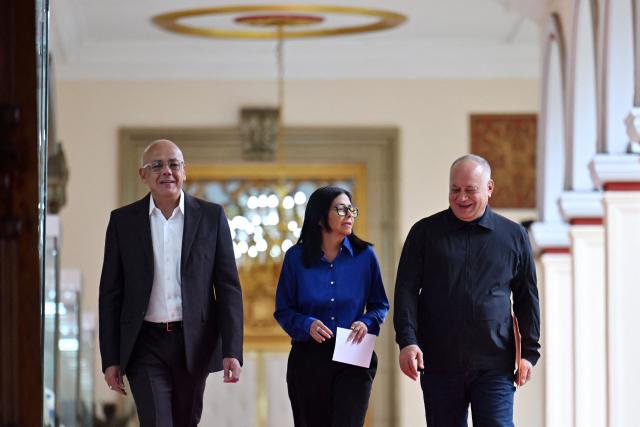 Venezuela's interim President Delcy Rodriguez (C), President of the National Assembly Jorge Rodriguez (L), and Minister of the Popular Power for Interior Diosdado Cabello walk in a hallway to arrive at a press conference at the Miraflores Presidential Palace in Caracas on January 14, 2026. Venezuela has freed 15 journalists, including a leading opposition figure, as the slow release of political prisoners begun after Nicolas Maduro's ouster continues, activists said on January 14. (Photo by Juan BARRETO / AFP)