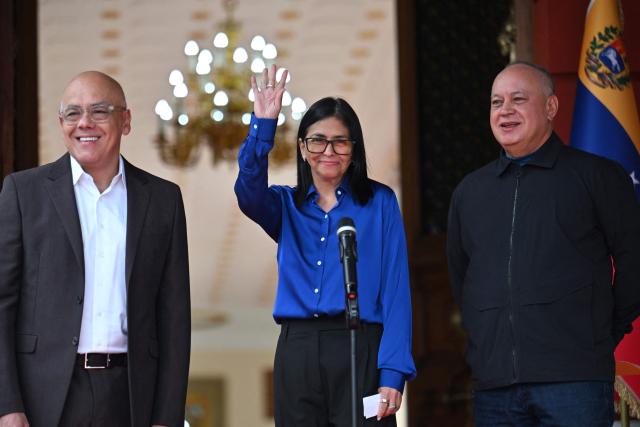 Venezuela's interim President Delcy Rodriguez (C) waves next to President of the National Assembly Jorge Rodriguez (L) and Minister of the Popular Power for Interior Diosdado Cabello after a press conference at the Miraflores Presidential Palace in Caracas on January 14, 2026. Venezuela has freed 15 journalists, including a leading opposition figure, as the slow release of political prisoners begun after Nicolas Maduro's ouster continues, activists said on January 14. (Photo by Juan BARRETO / AFP)