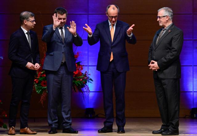 Saxony-Anhalt's incoming State Premier Sven Schulze (2nd L) and German Chancellor Friedrich Merz (2nd R) wave goodbye to the audience as Sascha Glaesser (L), president of Halle's Chamber of Commerce and Industry and Thomas Keindorf (R), president of Halle's chamber of crafts look on at the end of the New Year’s reception the Chamber of Commerce and Industry in Halle, eastern Germany on January 14, 2026. (Photo by John MACDOUGALL / AFP)