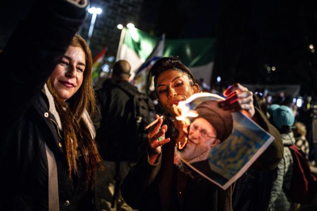 A woman burns a portrait of Iran's Supreme Leader, Ayatollah Ali Khamenei after lighting a cigarette during a demonstration in solidarity with Iranian protestors, in Israel's central city of Holon on January 14, 2026. Iran's long-time foe Israel has openly backed the protesters and expressed optimism about possible regime change, without suggesting it would intervene. (Photo by JOHN WESSELS / AFP)