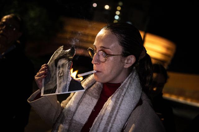 A woman burns a portrait of Iran's Supreme Leader, Ayatollah Ali Khamenei after lighting a cigarette during a demonstration in solidarity with Iranian protestors, in Israel's central city of Holon on January 14, 2026. Iran's long-time foe Israel has openly backed the protesters and expressed optimism about possible regime change, without suggesting it would intervene. (Photo by John Wessels / AFP)