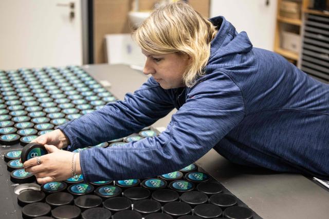 An employee of the Czech company Gufex producing ice hockey pucks for the 2026 Olympic Games handles freshly baked ice hockey pucks at the factory in the village of Katerinice, eastern Czech Republic, on December 10, 2025. The Gufex family company produces the black rubber discs for the Milan-Cortina Olympic Winter Games. Milan-Cortina is getting 10,000 pucks for the men's, women's and Paralympic tournaments and another 10,000 souvenir pucks. (Photo by Michal Cizek / AFP)