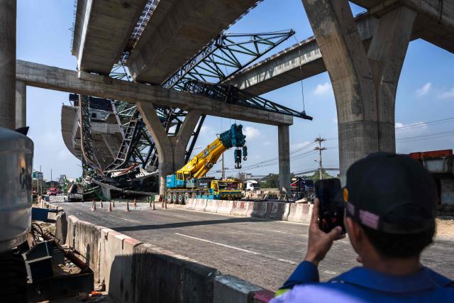 TOPSHOT - A recovery worker takes pictures at the site of a construction crane collapse onto a highway in Samut Sakhon on the outskirts of Bangkok on January 15, 2026. A crane at a highway construction site in the Bangkok suburbs collapsed on January 15, killing two people, a local police chief told AFP, one day after a crane fell on a train in Thailand, killing 32. (Photo by Chanakarn Laosarakham / AFP)