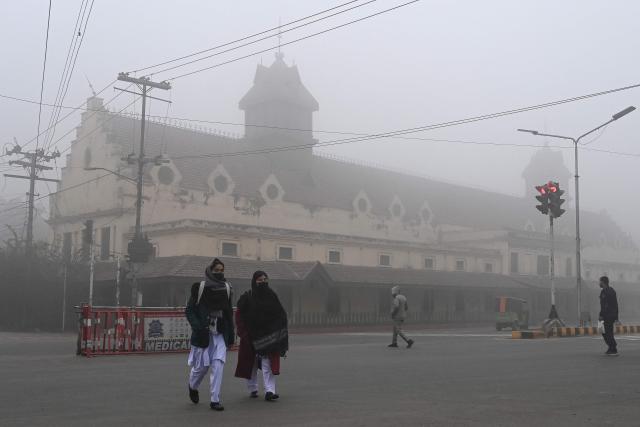 Women walk across a road amid dense fog on a cold winter morning in Lahore on January 15, 2026. (Photo by Arif ALI / AFP)