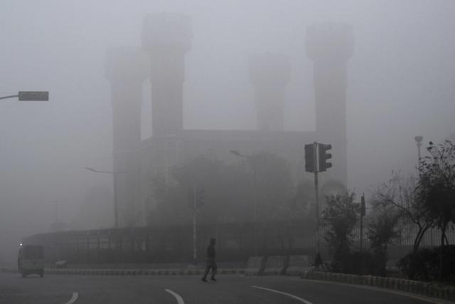 Commuters travel along a road engulfed in dense fog on a cold winter morning in Lahore on January 15, 2026. (Photo by Arif ALI / AFP)