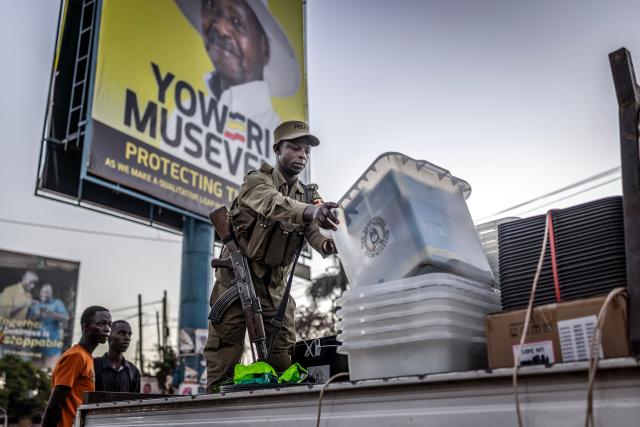 A Ugandan police officer unloads ballot boxes from a truck at a polling station set up in front of an electoral billboard supporting Uganda’s incumbent president and National Resistance Movement (NRM) presidential candidate Yoweri Museveni in Kampala on January 15, 2026, during Uganda’s 2026 general elections. (Photo by Luis TATO / AFP)
