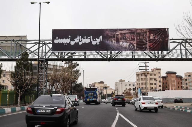 Cars drive under a banner that reads "This is not a protest" in Tehran on January 15, 2026. A protest movement across Iran, initially sparked by economic grievances, has turned into one of the biggest challenges yet to the clerical leadership since it took power in 1979. (Photo by ATTA KENARE / AFP)