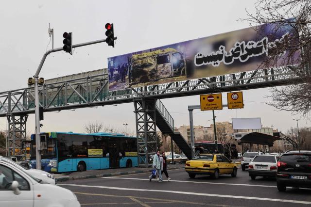 Cars drive under a banner that reads "This is not a protest" in Tehran on January 15, 2026. A protest movement across Iran, initially sparked by economic grievances, has turned into one of the biggest challenges yet to the clerical leadership since it took power in 1979. (Photo by ATTA KENARE / AFP)