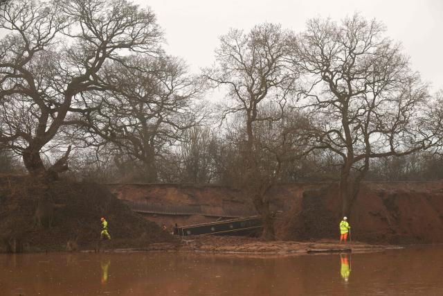 A construction workers stand near a stranded canal boat, in Whitchurch, north-west England, on January 15, 2026. On December 22, 2025 Llangollen Canal collapsed, blamed on "embankment failure" by engineers, leaving narrowboat owners without their homes over Christmas. (Photo by Oli SCARFF / AFP)