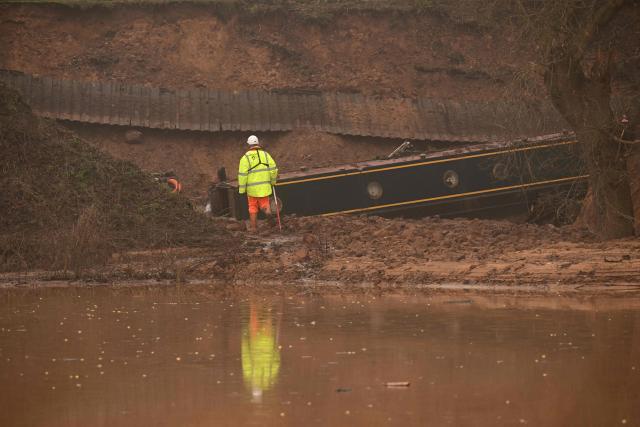 A construction worker looks at a stranded canal boat, in Whitchurch, north-west England, on January 15, 2026. On December 22, 2025 Llangollen Canal collapsed, blamed on "embankment failure" by engineers, leaving narrowboat owners without their homes over Christmas. (Photo by Oli SCARFF / AFP)