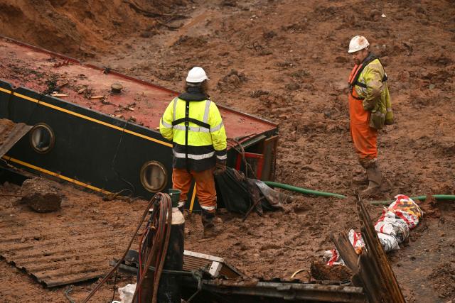 Construction workers look at a stranded canal boat, in Whitchurch, north-west England, on January 15, 2026. On December 22, 2025 Llangollen Canal collapsed, blamed on "embankment failure" by engineers, leaving narrowboat owners without their homes over Christmas. (Photo by Oli SCARFF / AFP)
