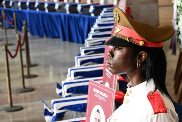 TOPSHOT - A Cuban guard of the Ceremonial Battalion stands next to the caskets during the funeral honors of the 32 Cuban soldiers who died during the US incursion to capture Venezuelan leader Nicolas Maduro, at the Ministry of the Revolutionary Armed Forces in Havana on January 15, 2026. The capture by US forces of Venezuelan leader Nicolas Maduro on January 3, 2026, and the killing in the operation of 32 Cubans assigned to protect him represent a major blow for the island's revered intelligence services, experts say. (Photo by Yamil LAGE / AFP)