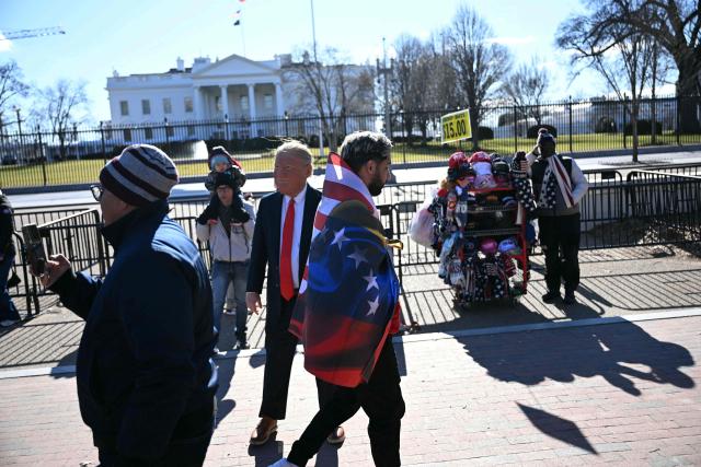 A supporter of the Venezuelan opposition walks past a man dressed as US President Donald Trump during a demonstration outside the White House as Trump meets with Venezuelan opposition leader Maria Corina Machado in Washington, DC, on January 15, 2026. (Photo by Brendan SMIALOWSKI / AFP)
